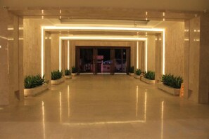 A spacious lobby with a polished floor, a central entrance, and potted plants.