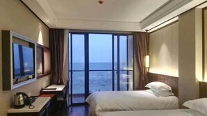Une chambre d’hôtel avec deux lits, une télévision, un bureau avec une bouilloire et une grande fenêtre donnant sur un beau paysage.