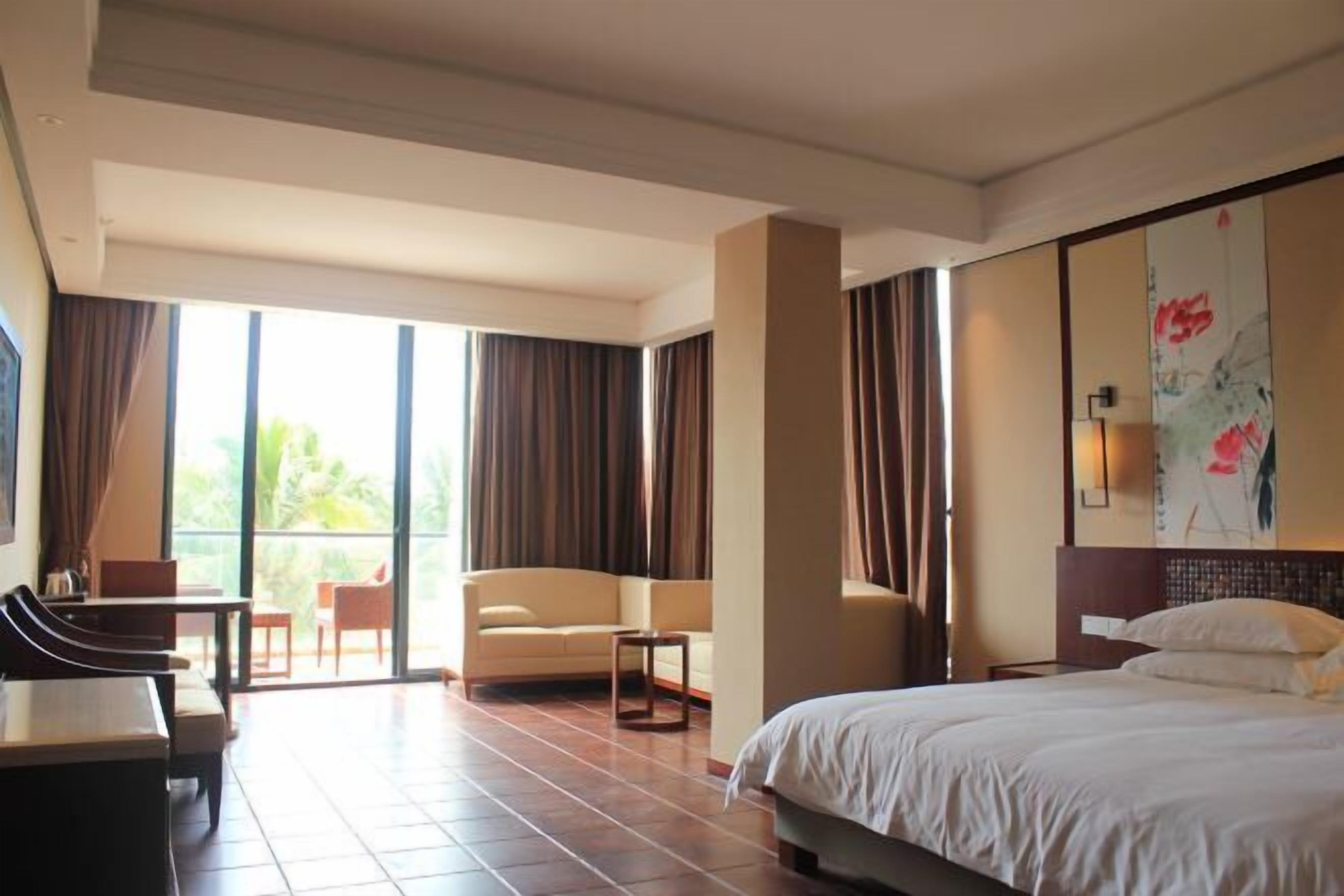 A hotel room with a bed, a sofa, a desk, and a balcony with curtains.
