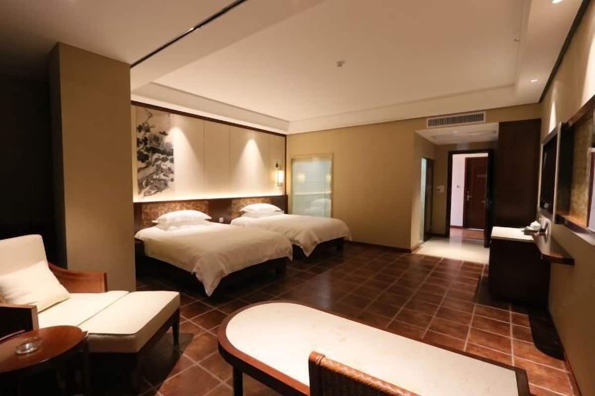 Hotellihuone, jossa on kaksi sänkyä, oleskelualue tuolilla ja pöydällä sekä suuri peili.
