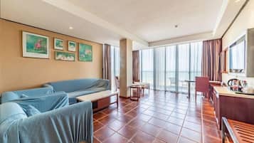 Una habitación de hotel con cama, zona de estar, mesa de comedor y un ventanal grande.