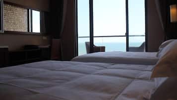 A hotel room with two beds, a large window with a view of the sea, and a small table.