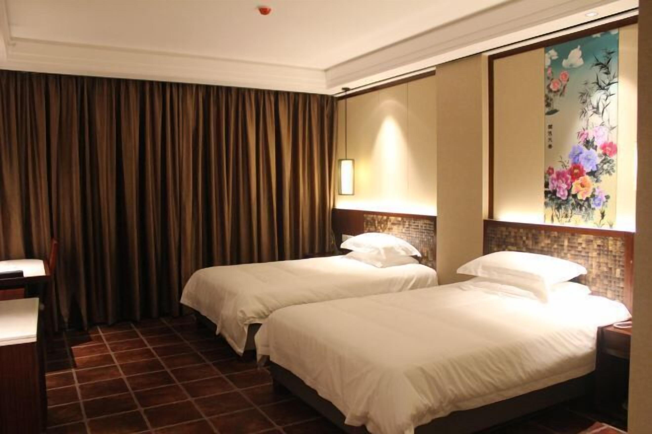 Habitación de hotel con dos camas, un escritorio, una silla, un cuadro grande en la pared y una cortina.