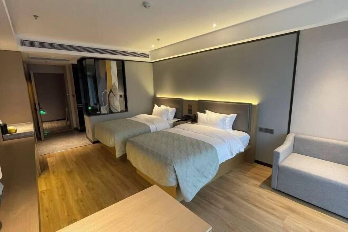 Ein Hotelzimmer mit zwei Betten, einer Couch, einem Holzboden und einem Spiegel.