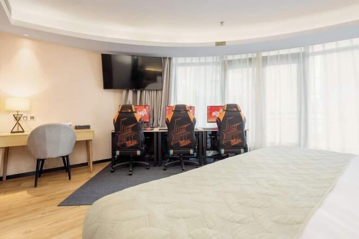 Ein Hotelzimmer mit einem großen Bett, einem Schreibtisch mit zwei Stühlen, einem Flachbildfernseher und einem Fenster mit Vorhängen.