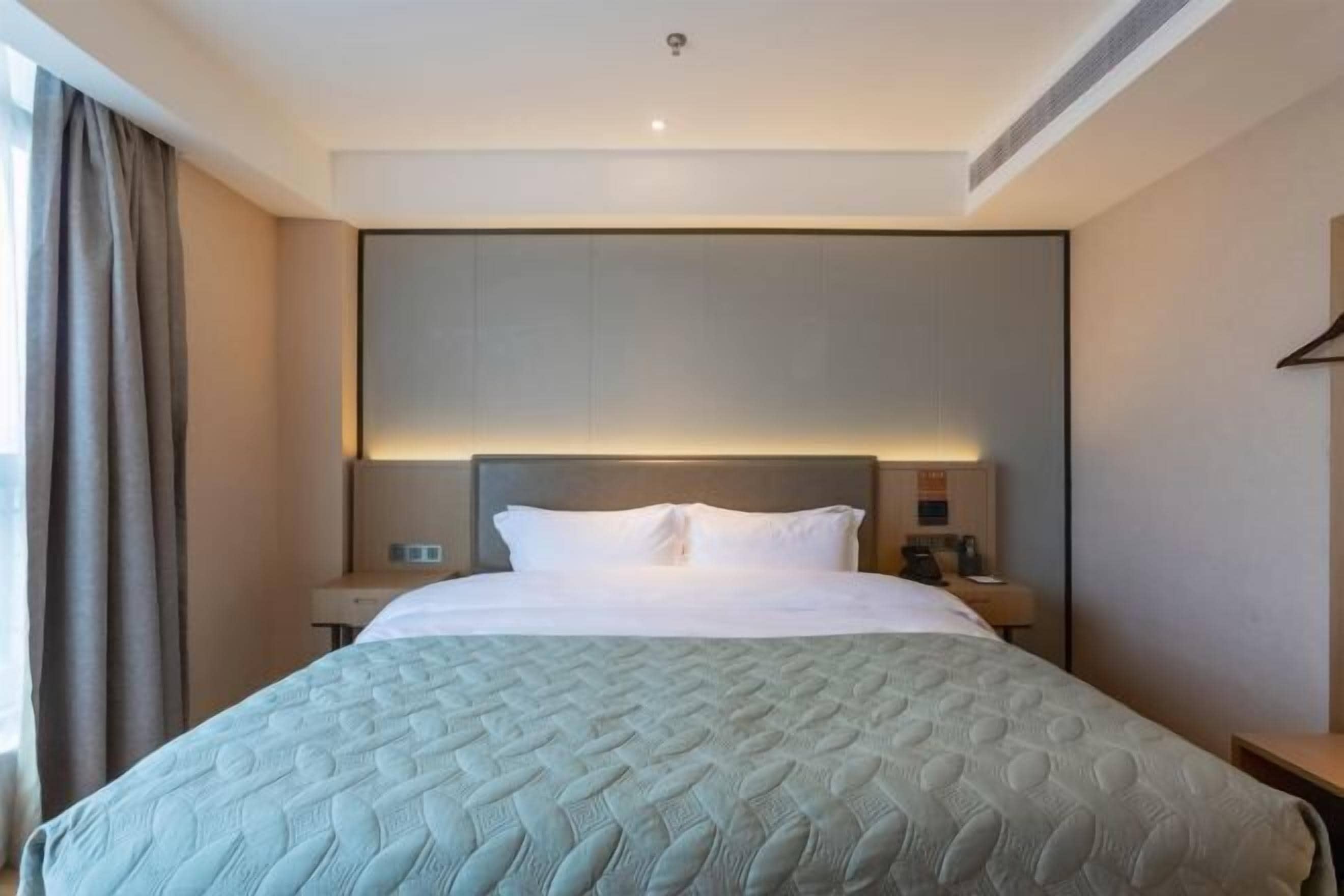 A hotel room with a bed, bedside tables, a headboard, and a window with curtains.