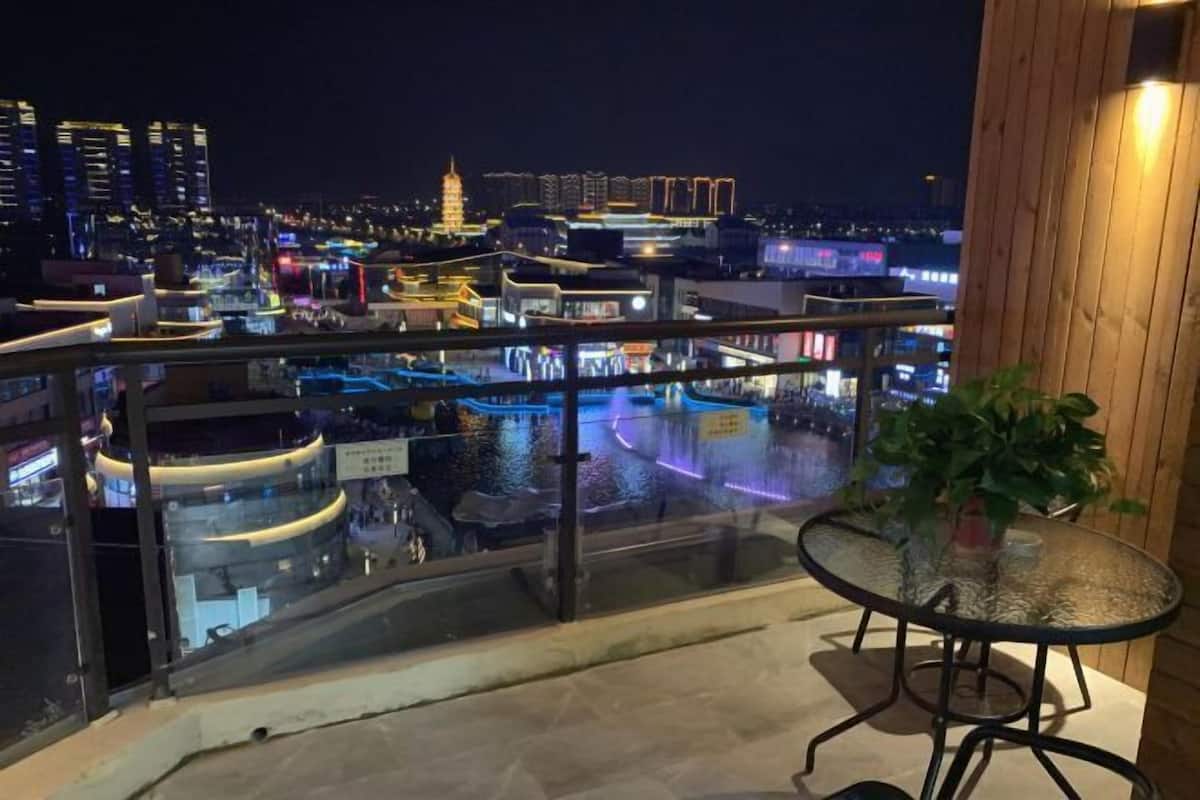 Ein Balkon mit Glasgeländer und Blick auf eine beleuchtete Stadt bei Nacht.