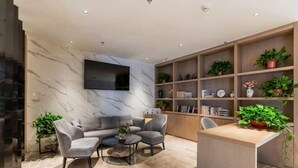 A modern living room with a marble wall, a sofa, two armchairs, a coffee table, and a TV. There are shelves with plants and books. - Gya Hotel (Nantong Nanshanhu Shuijie) (Nantong)