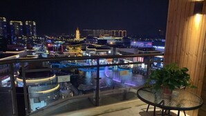 A balcony with a glass railing overlooking a cityscape at night, featuring illuminated buildings and a river. - Gya Hotel (Nantong Nanshanhu Shuijie) (Nantong)