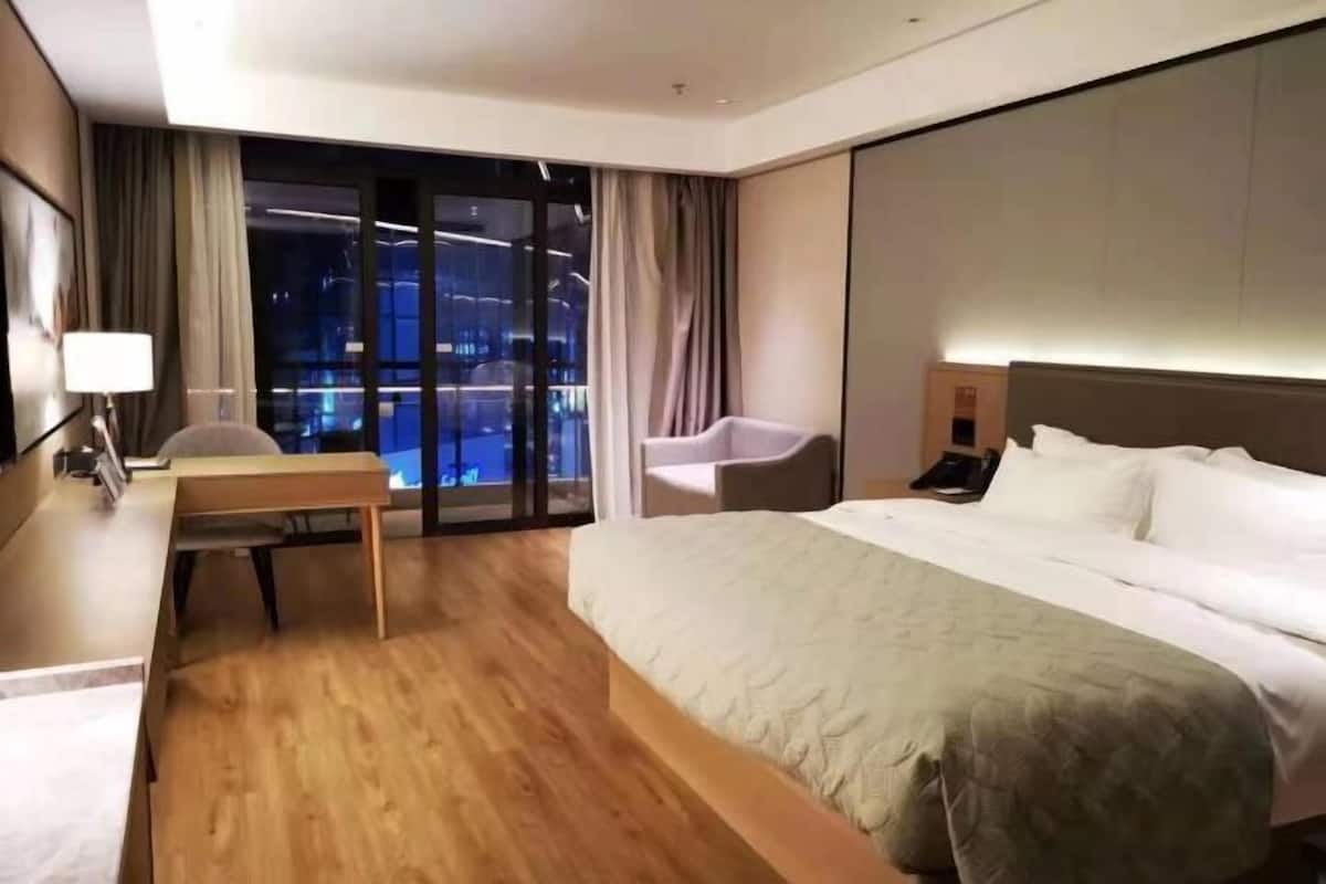 Ein modernes Hotelzimmer mit einem großen Bett, einem Schreibtisch, einem Sessel und Blick auf die beleuchtete Stadt.