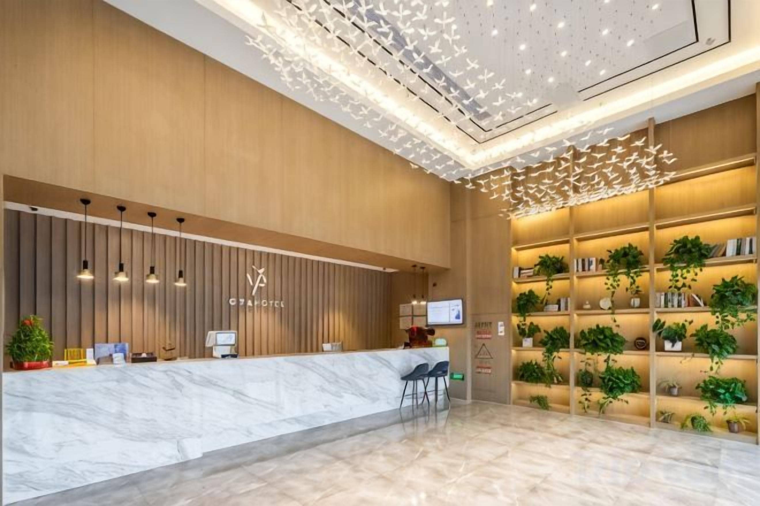 A hotel reception area with a marble counter, wall-mounted TVs, and a ceiling with a geometric light fixture.