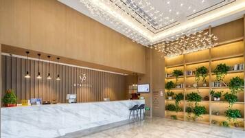 A hotel reception area with a marble counter, wall-mounted TVs, and a ceiling with a geometric light fixture.