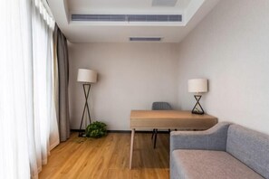 Ein modernes Hotelzimmer mit Holzboden, grauem Sofa, kleinem Tisch, zwei Lampen und einer Pflanze.