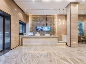 Un moderno mostrador de recepción con un televisor de pantalla plana grande, paneles de madera e iluminación colgante.