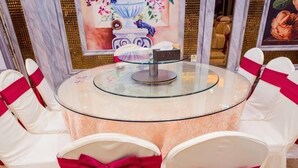 Une table ronde en verre, recouverte d’une nappe blanche, entourée de chaises blanches ornées de rubans rouges.