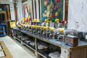 A buffet setup with multiple food stations, a marble wall, and a blue cart. - Duxiu Hotel (Tacheng City)