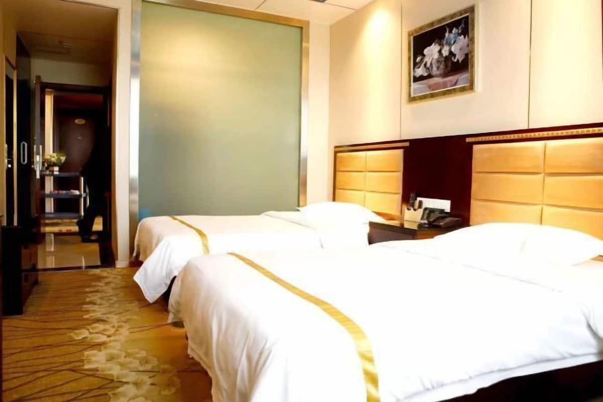 A hotel room with two beds, a nightstand, a lamp, and a framed picture on the wall.