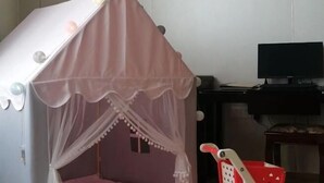 Une tente de jeu pour enfants, dotée d’un auvent, avec un panier rouge et un téléviseur visible au fond.
