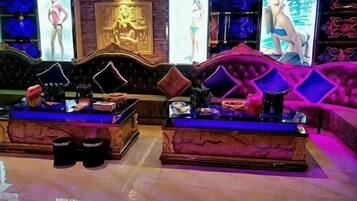 Un lobby lujoso con piso de mármol, una zona de estar central con una chaise longue y una gran pared decorativa con obras de arte.