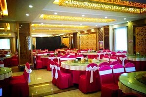 A banquet hall with round tables and chairs, some with white sashes. - Duxiu Hotel (Tacheng City)