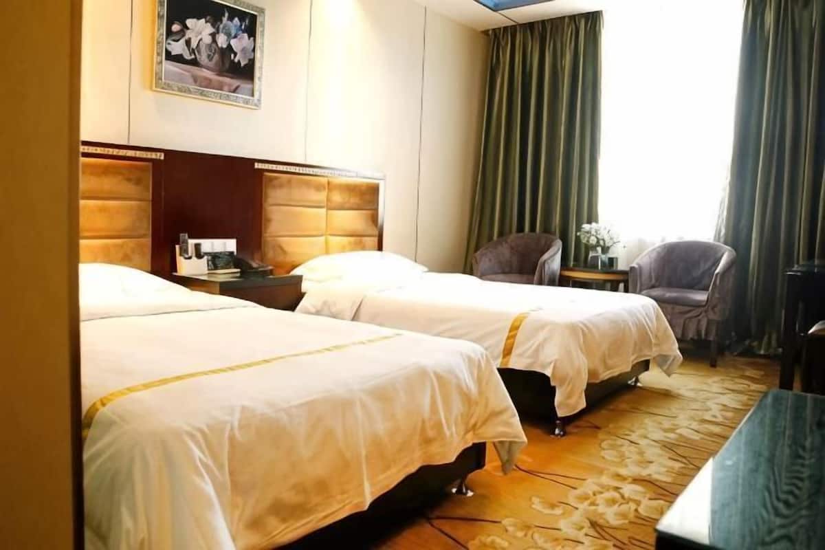 A hotel room with two beds, a nightstand, a chair, and a view of the outdoors.