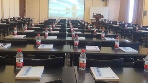 Une salle de conférence avec des rangées de tables, chacune étant équipée d’un carnet, d’une bouteille d’eau et d’un badge nominatif.