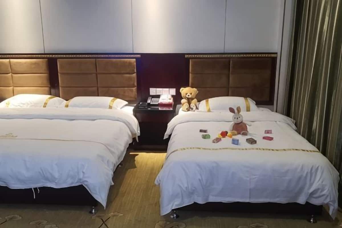 A hotel room with two beds, a nightstand, a teddy bear, and a small table with items on it.