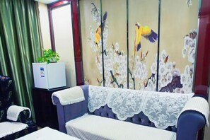 A room with a sofa covered in a lace throw, a small plant on a cabinet, and a wall with floral artwork. - Duxiu Hotel (Tacheng City)