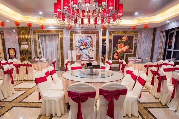A banquet hall with round tables, white chairs with red sashes, and a central chandelier. - Duxiu Hotel (Tacheng City)