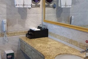 Ein Badezimmer mit Marmorplatte, Waschbecken, Spiegel mit goldener Rahmung und Telefon.