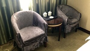 Deux fauteuils et une petite table ronde avec un plateau, placés près d’une fenêtre ornée de rideaux.