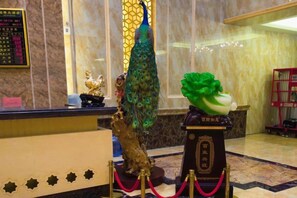 A reception desk with a peacock statue, a green and white sculpture, and a display case with a golden figure. - Duxiu Hotel (Tacheng City)