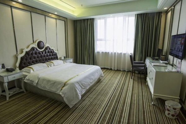Una habitación de hotel con una cama grande, un escritorio con una silla, un televisor y una ventana con cortinas.