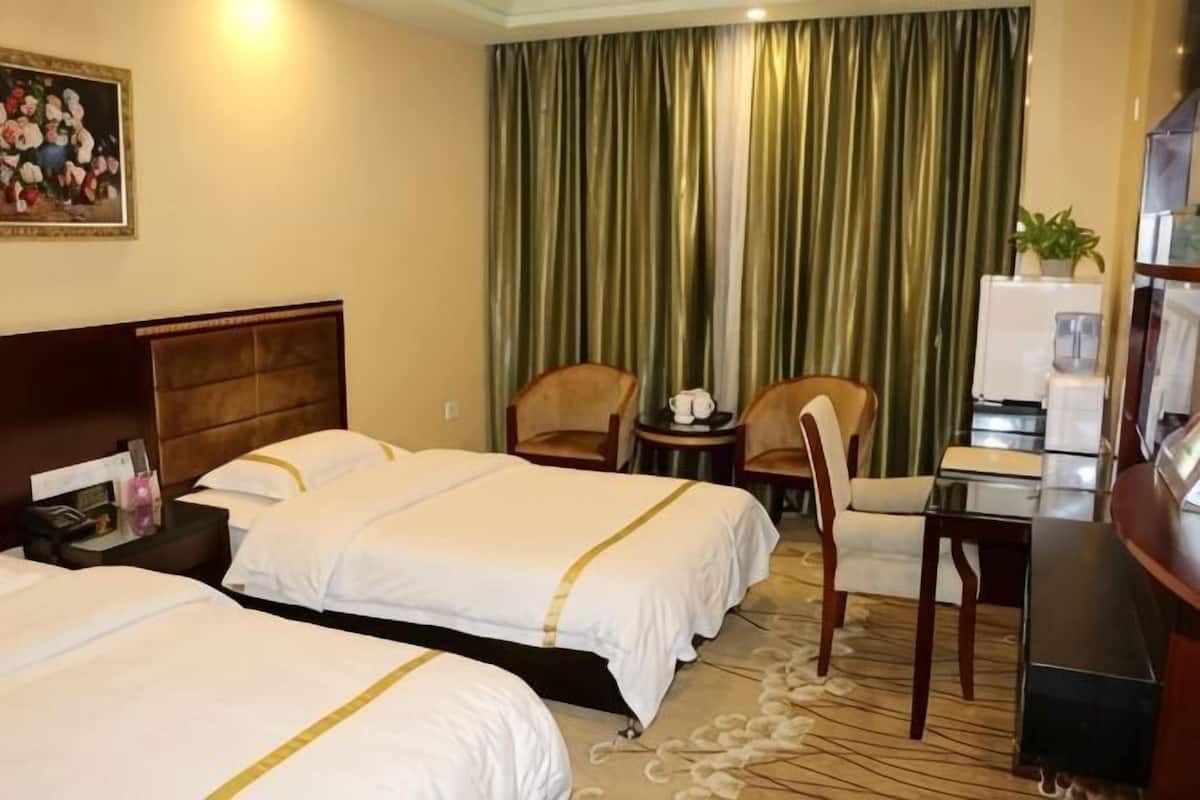 A hotel room with two beds, a desk, chairs, a painting, and a curtain.