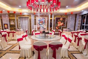 Une salle de banquet avec des tables rondes et des chaises, un lustre et un tableau représentant des fleurs.