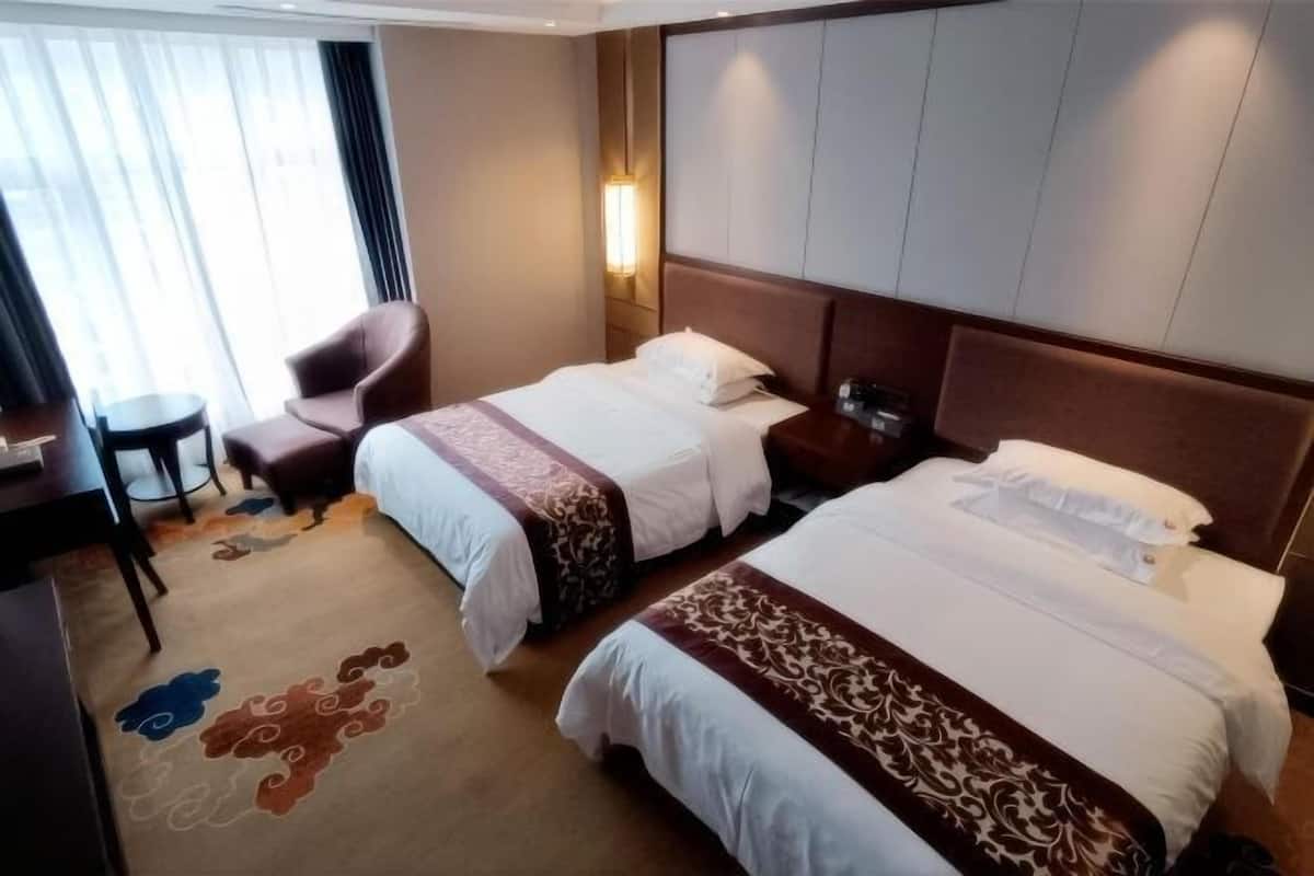 A hotel room with two beds, a desk, a chair, and a small table.