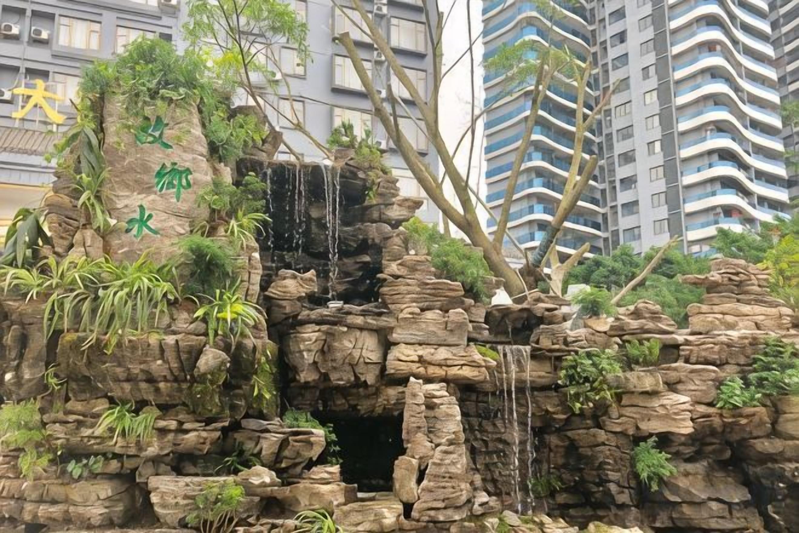 A rock formation with a waterfall and greenery, surrounded by high-rise buildings.