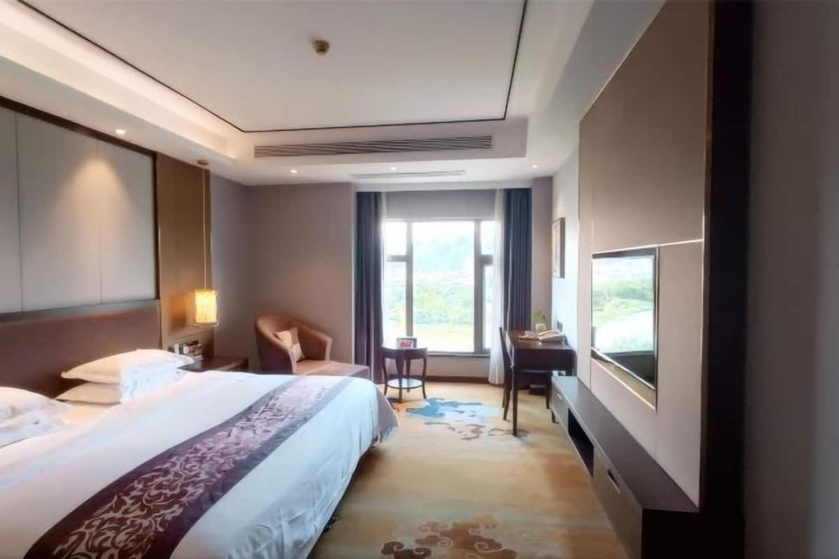 A hotel room with a bed, a desk, a chair, a TV, and a window with a view.