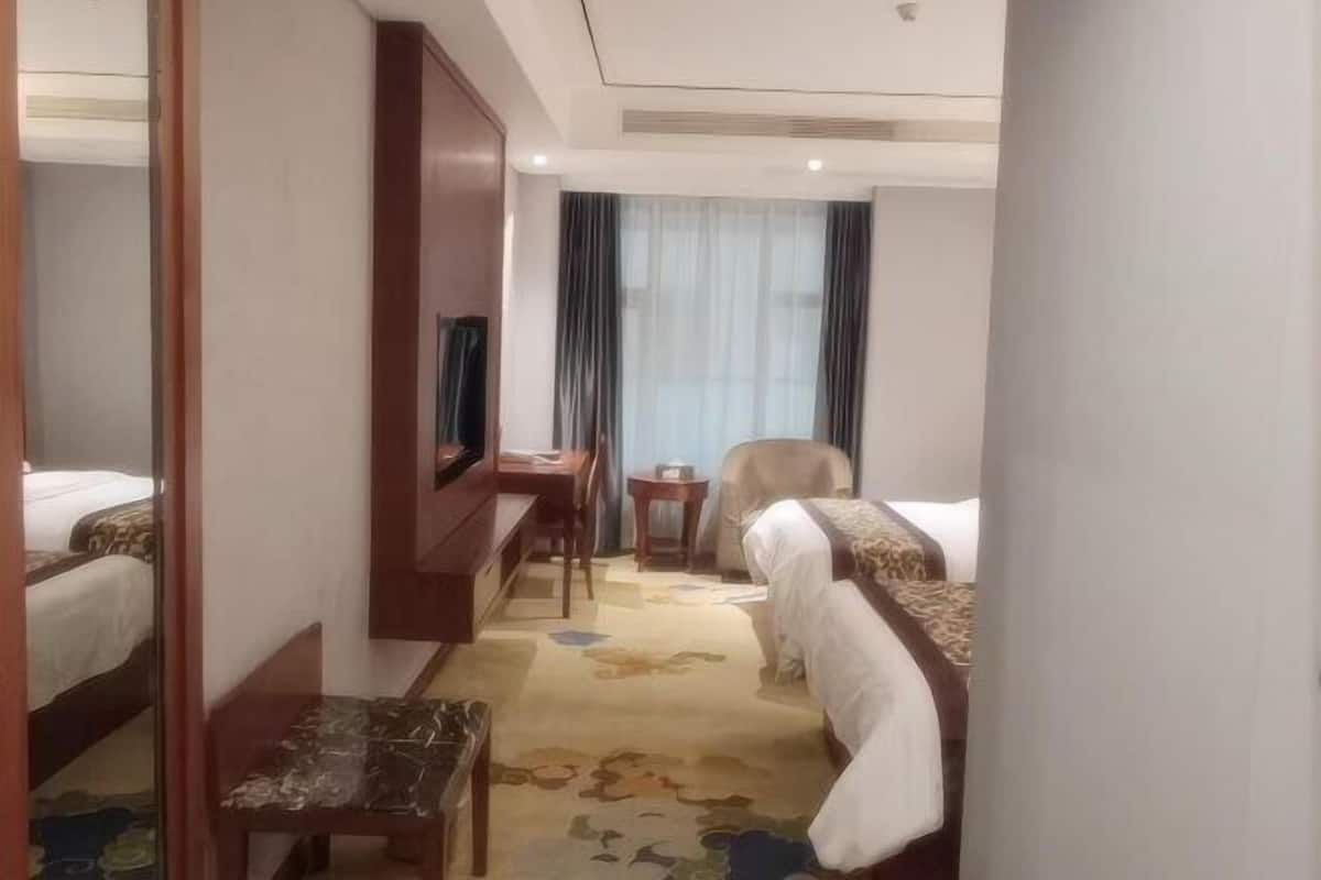 A hotel room with two beds, a desk, a chair, a television, and a small table.