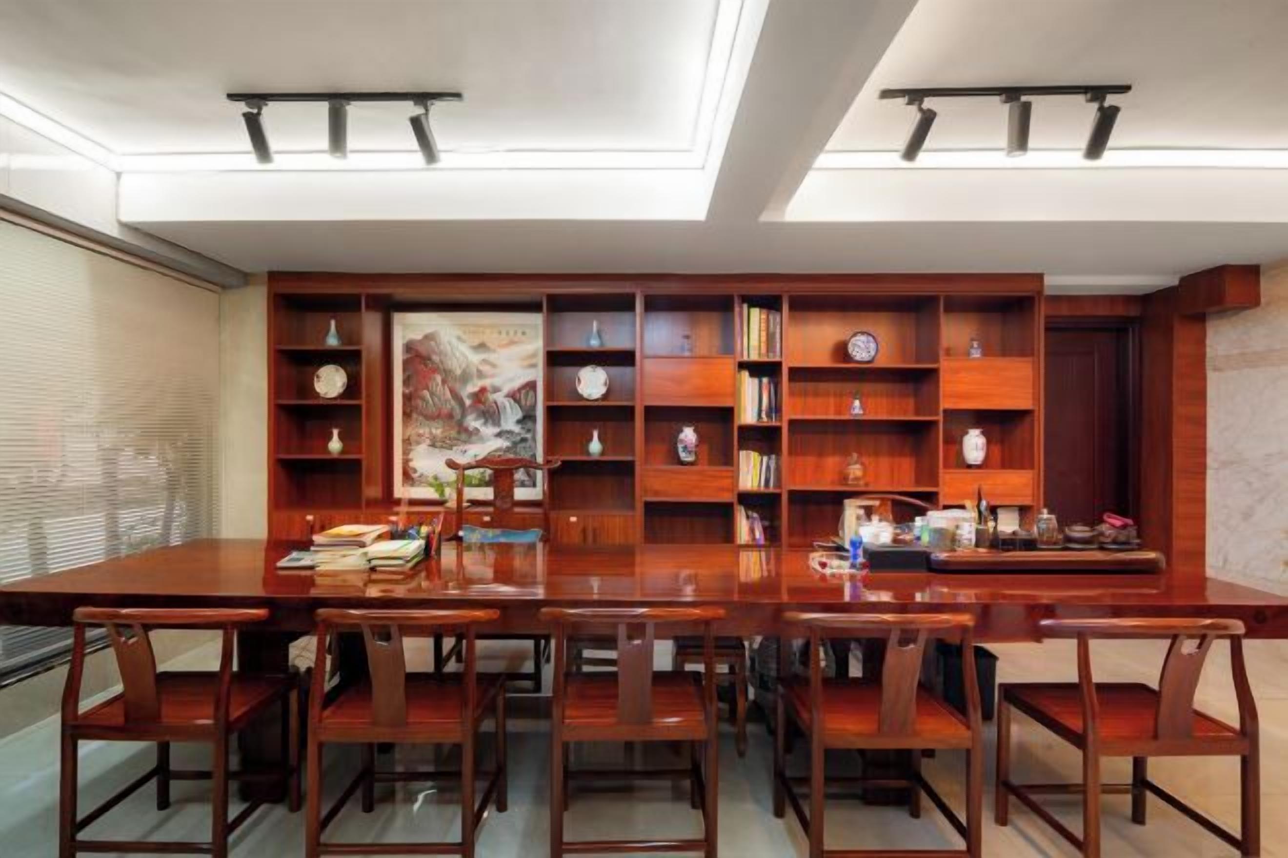A dining area with a long wooden table and chairs, surrounded by wooden bookshelves filled with books and decorative items.