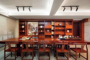 A dining area with a long wooden table and chairs, surrounded by wooden bookshelves filled with books and decorative items. - Foshan Convergence Fashion Hotel (Foshan)