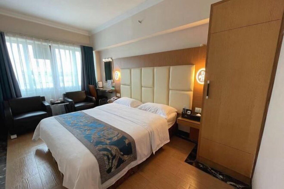 A hotel room with a large bed, a desk, a chair, a wardrobe, and a window with curtains.