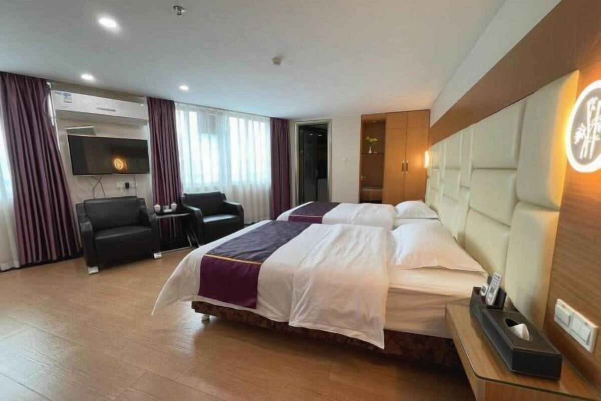 A hotel room with two beds, a sofa, a TV, and a minibar.