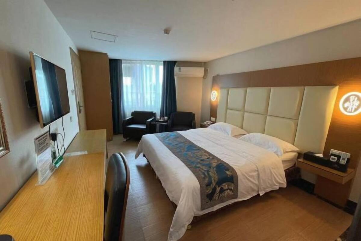 A hotel room with a bed, a desk, a chair, a TV, and a window with curtains.