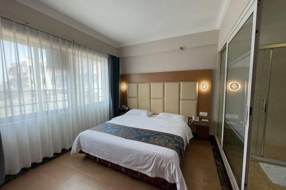 A hotel room with a large bed, a wooden headboard, a bedside table with a lamp, and a sliding glass door closet.