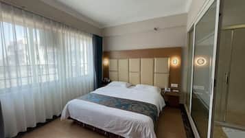 A hotel room with a large bed, a wooden headboard, a bedside table with a lamp, and a sliding glass door closet.