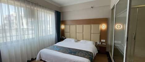 A hotel room with a large bed, a wooden headboard, a bedside table with a lamp, and a sliding glass door closet.