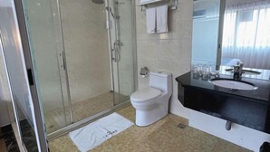 Une salle de bain moderne avec une douche à parois de verre, des toilettes blanches, un lavabo noir et un grand miroir.
