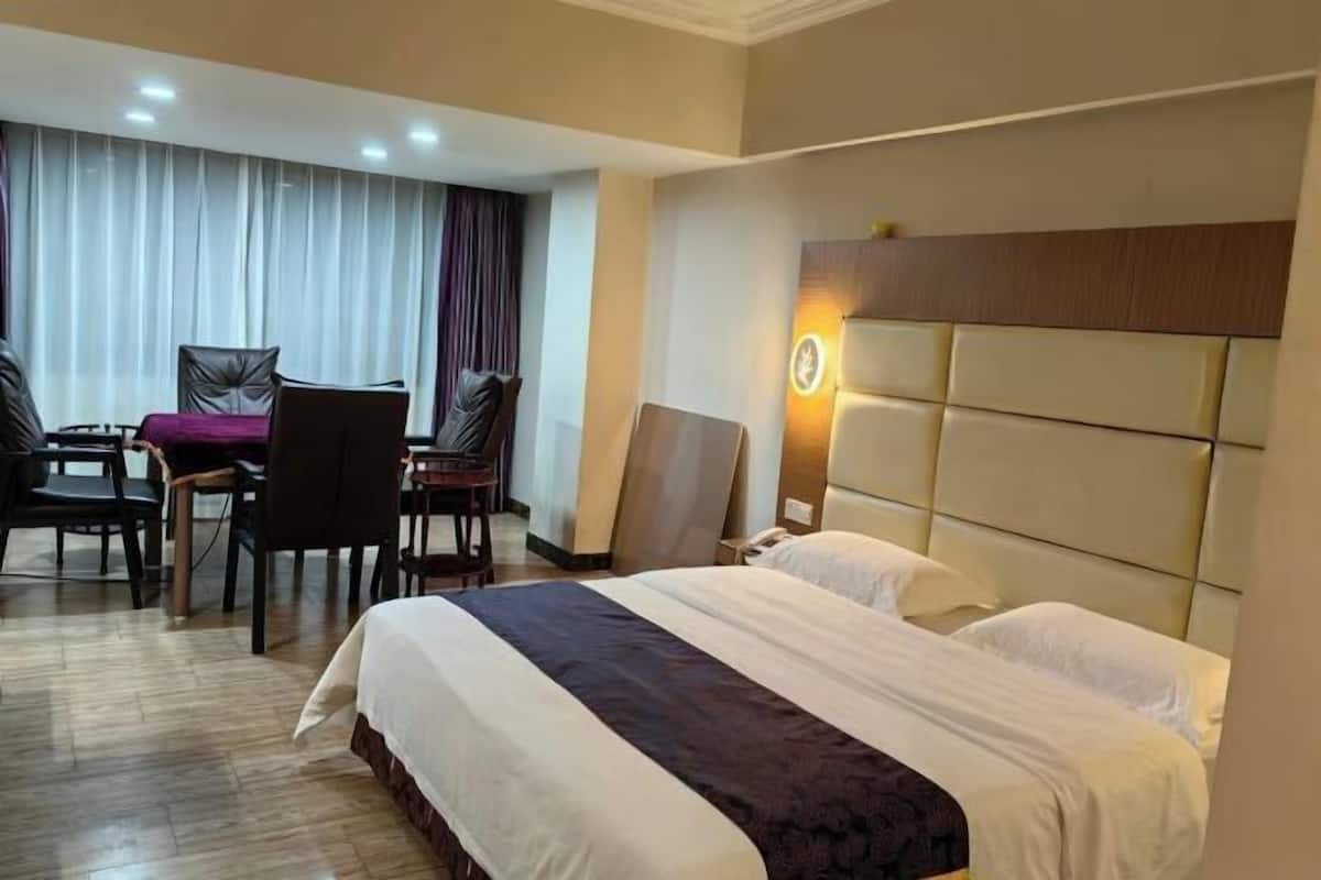 A hotel room with two beds, a dining area with a table and chairs, and a large padded headboard.