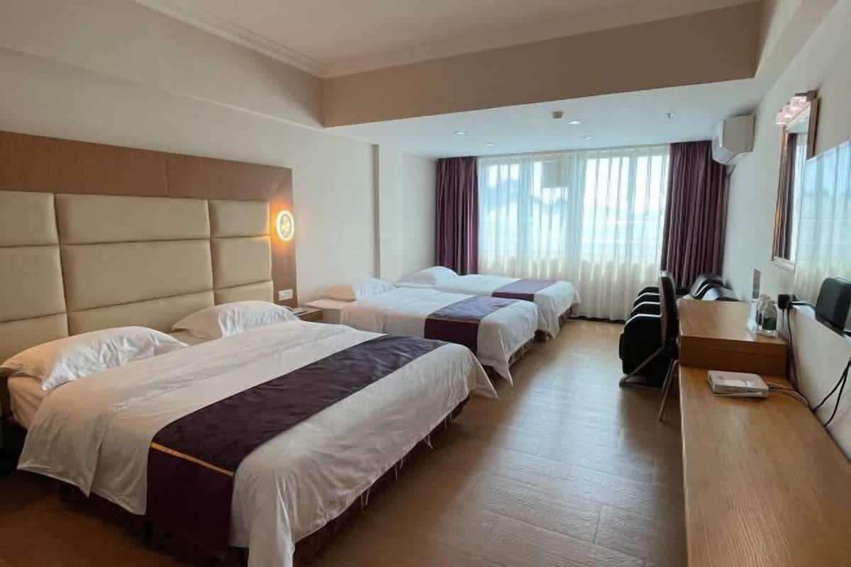 A hotel room with three beds, a desk, a chair, and a TV.